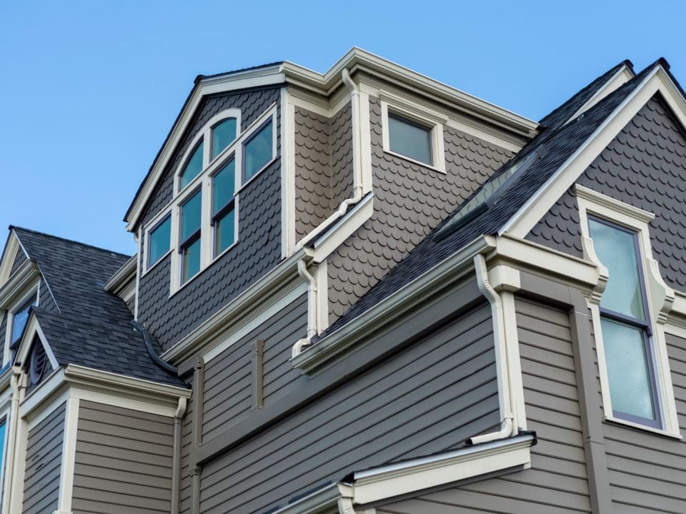 A large, historic home with grey siding in scallop and Dutch lap styles.