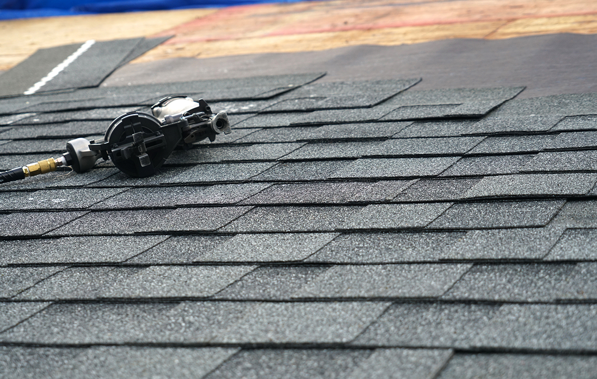 A close-up view of a nail-gun laying on a roof mid-installation