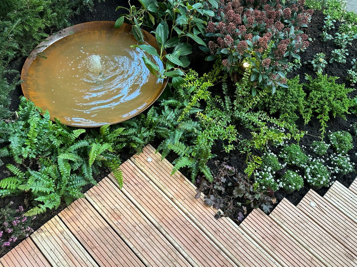 the edge of composite wooden deck boards that lead to a small garden with a fountain.