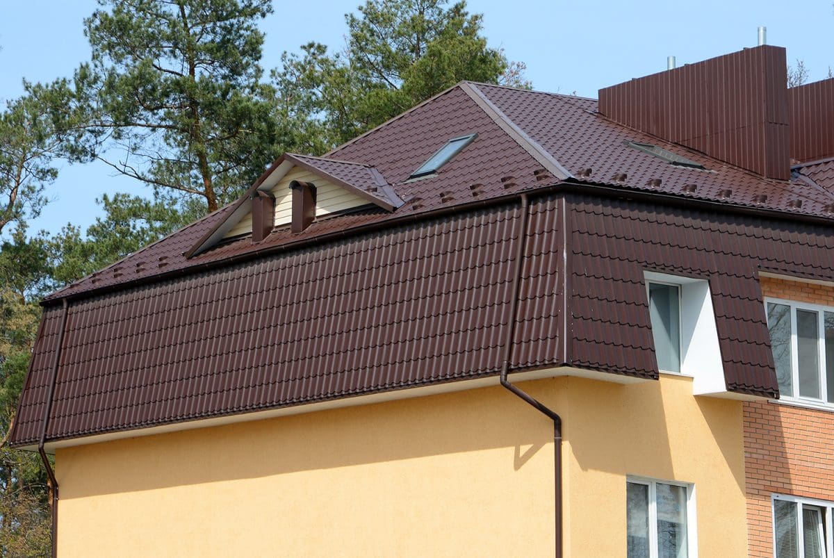 A brown mansard roofed home, roofed with clay tiles. 