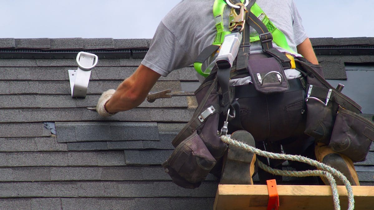 A roof worker wearing a safety harness as he patches a roof