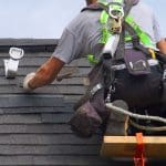 A roof worker wearing a safety harness as he patches a roof