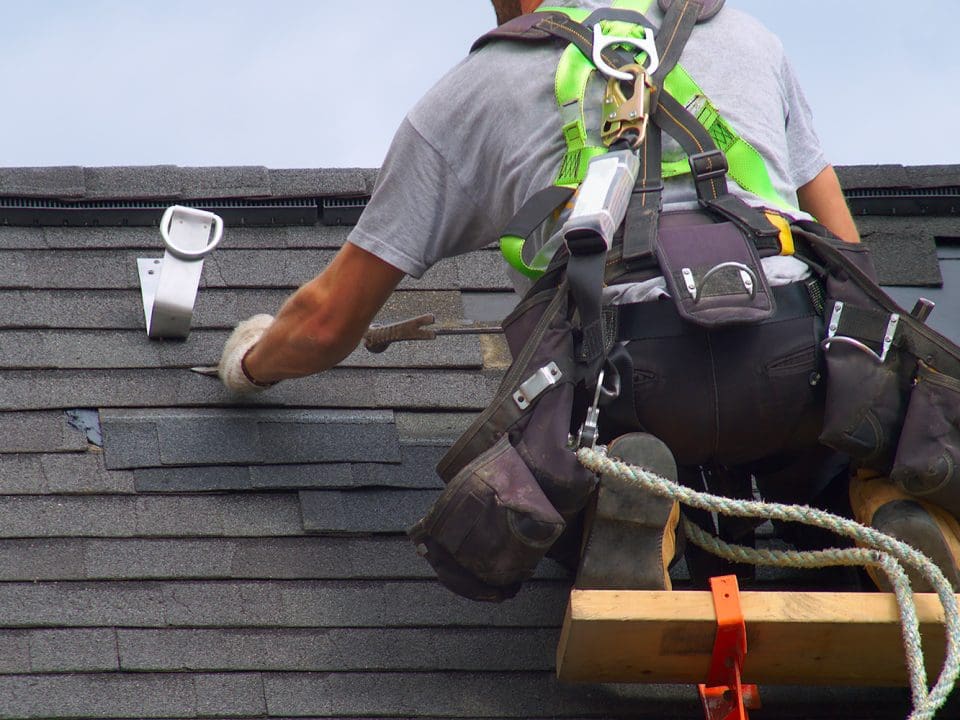 A roof worker wearing a safety harness as he patches a roof