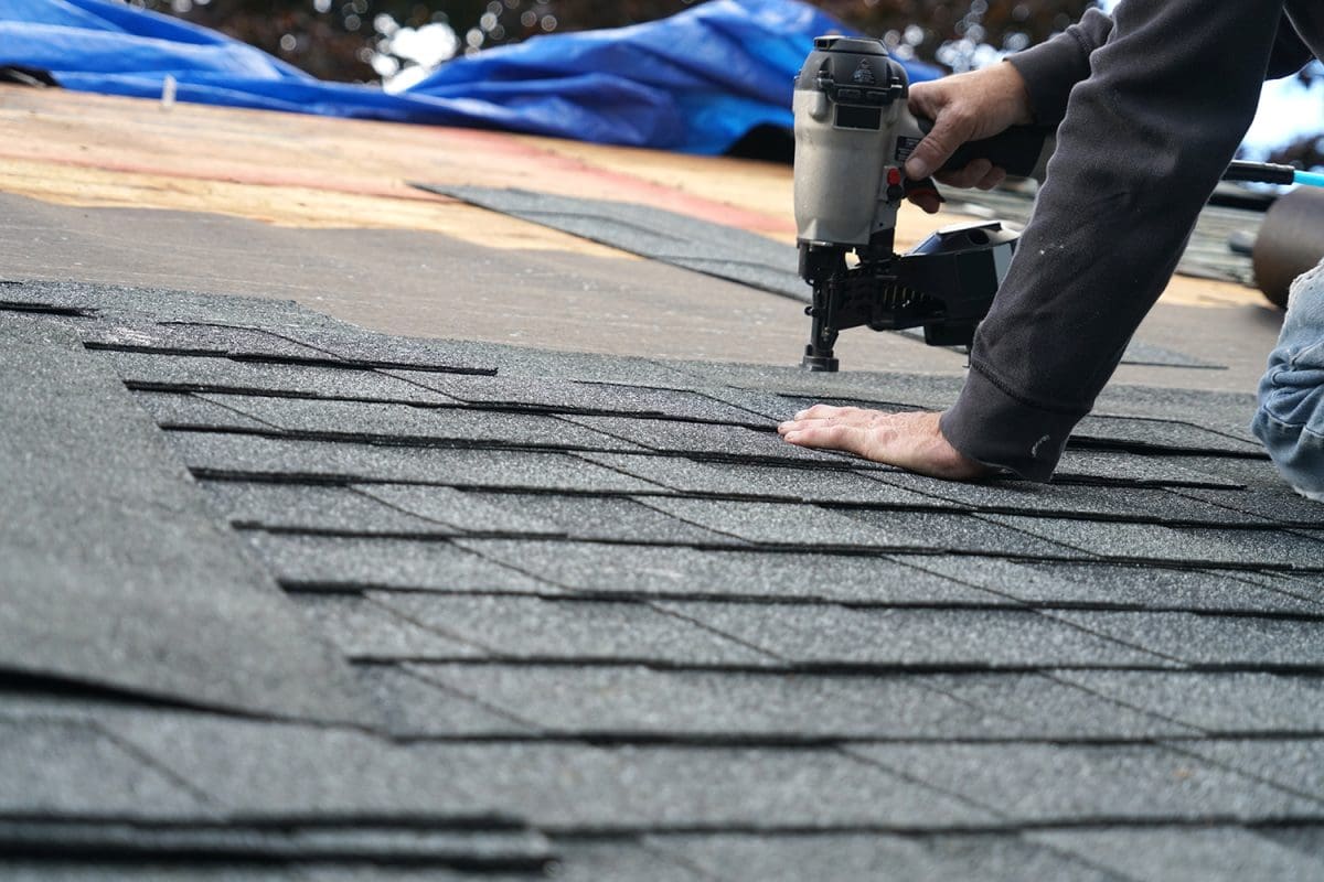 A roof repair contractor uses a nail gun to put shingles on a roof.