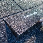 A closeup of a roof shingle being lifted off a roof to inspect it