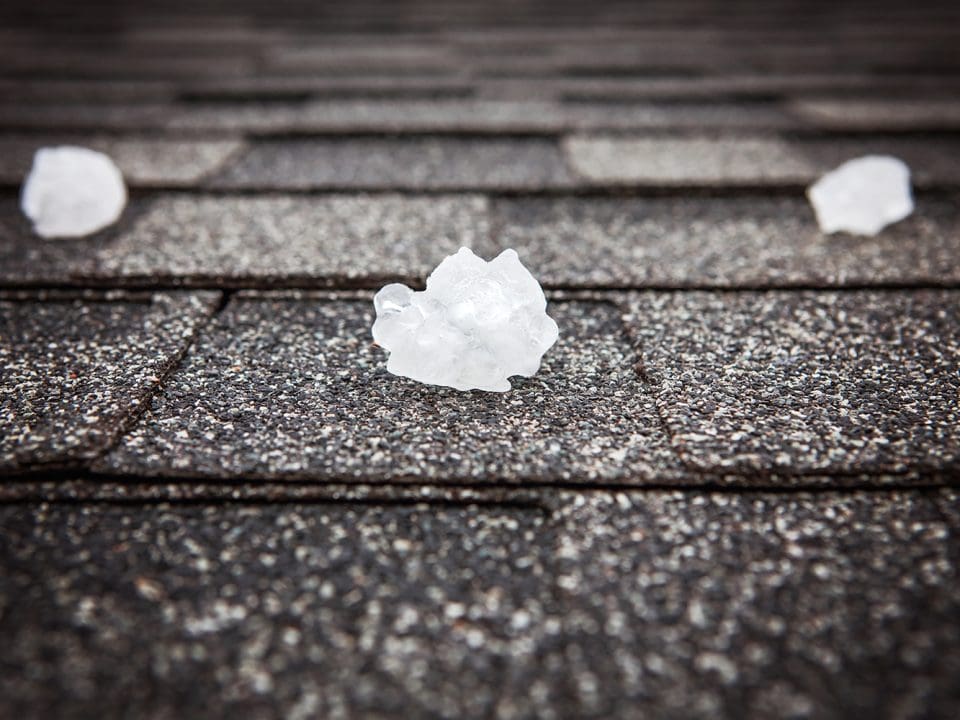 A close-up shot of a roof with hailstones sitting on the shingles