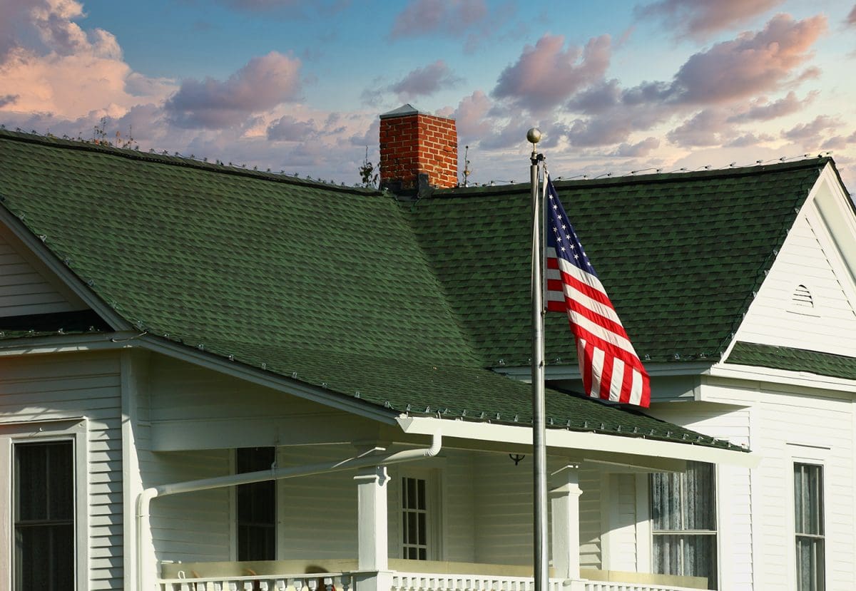 A small home with a green roof and an American flag